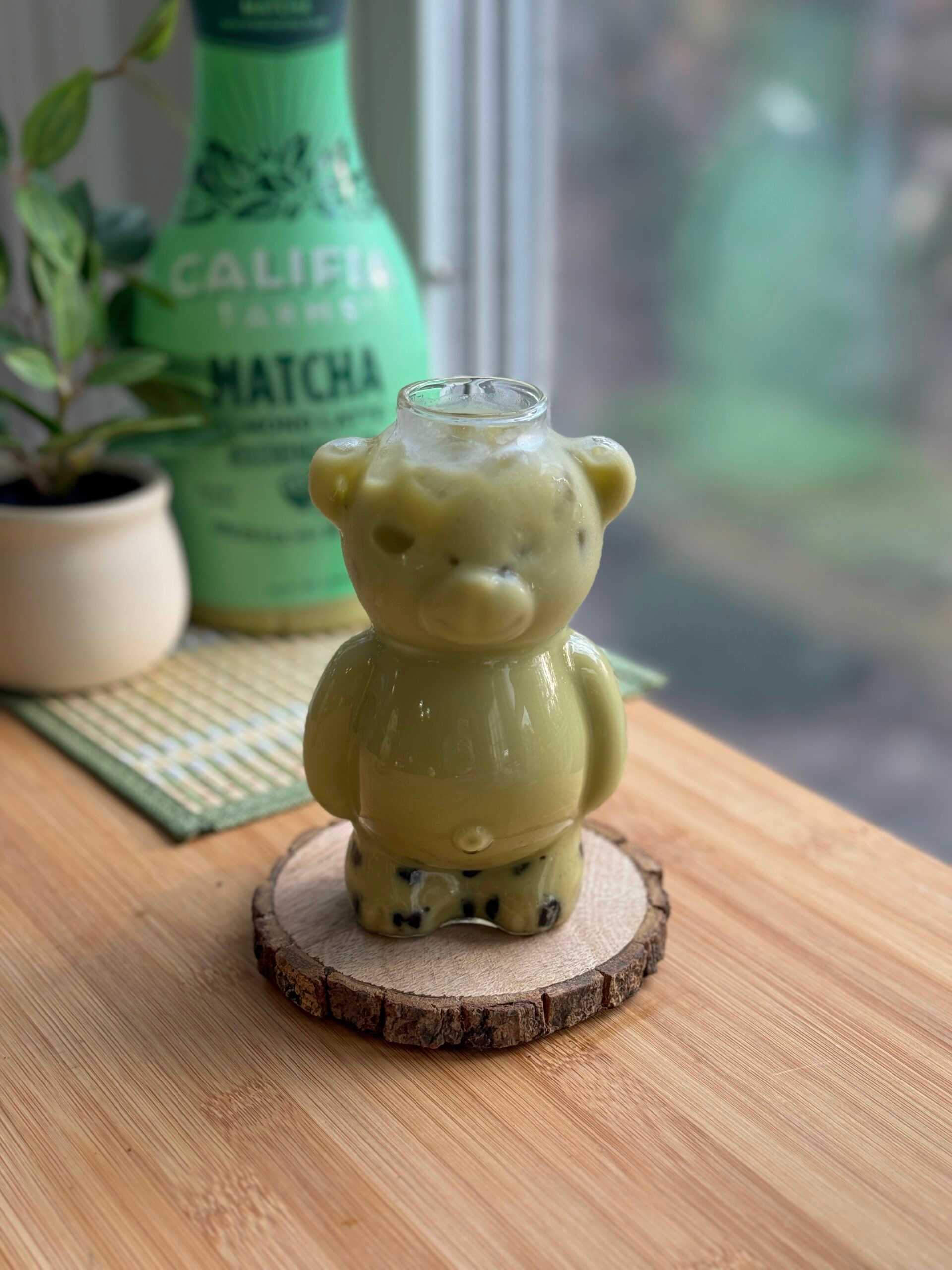 A bear-shaped glass sits at the front of the image, filled with an iced matcha latte with boba pearls
