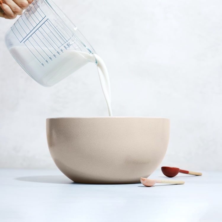 oat milk being poured into a bowl from a measuring cup